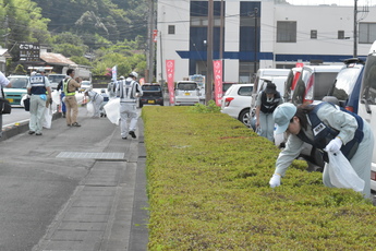 道の駅駐車場生垣と道路歩道を清掃する複数の参加職員