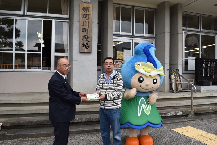 なかちゃんナンバープレートを交付する町長と受け取る町民の写真