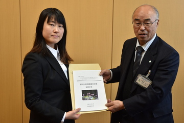 青年海外協力隊に参加する女性に冊子を渡す町長の写真