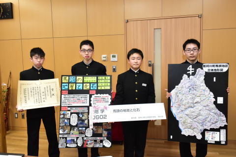 賞状と研究結果をまとめた展示物を持つ馬頭中理科部の生徒たちの写真