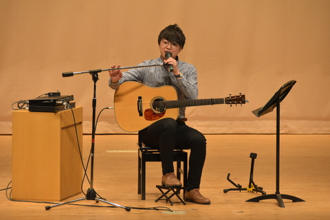 アコースティックギターを持って講演をしている男性の写真