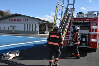 車体後部に降下した梯子を手作業で下す隊員2人の写真