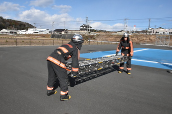 梯子の両端を持ち地面に置く隊員2人の写真