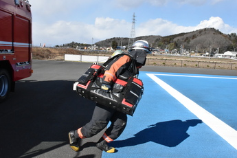消火活動時の装備で、ホースを収納したバッグを抱え走り出す隊員1人の写真