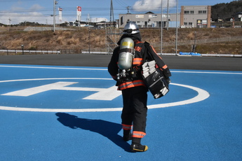 消火活動時の装備で、ホースを収納したバッグを抱えた隊員1人の後ろ姿の写真、ボンベを背負っている