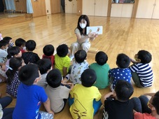 床に座る、わかあゆ認定こども園の園児たちに向き合って座り、英語の絵本を英語と日本語で教えている、パメラさんの写真