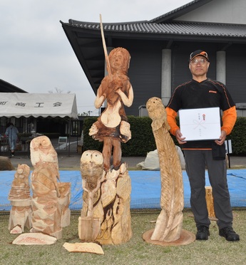 チェンソーカービングで作られたフクロウと少女の脇に立つ製作者の写真