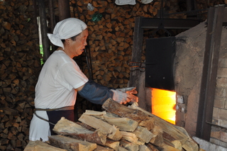 穴窯に薪をくべる岡さんの写真