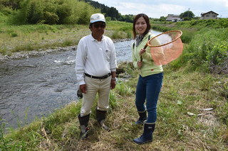 河原にいる男性と網を持った女性の写真