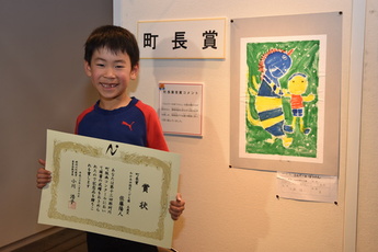 町長賞を受賞した作品と賞状を持つ子どもの写真