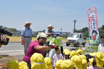 青壮年部の方が園児全員の前で、ジャイアントかぼちゃの苗を見せ説明している写真 青壮年部の方が園児全員の前で、ジャイアントかぼちゃの苗を見せ説明している写真