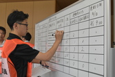 避難訓練でホワイトボードに避難・被害の状況を書き込んでいる写真