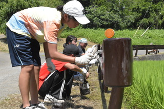 ガードレールをペンキで塗り替える高校生たちの写真