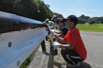 ガードレールにペンキで塗り替えをする高校生と棚田の風景の写真