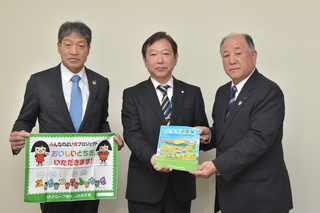 JAなす南から町内小学生へ寄贈するランチョンマットと教材を持つ3人の男性の写真