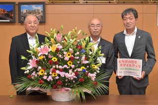 フラワーアレンジメントを前にした3人の男性の写真