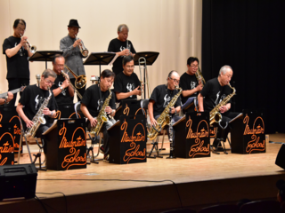 前列からサックス、トロンボーン、トランペットの演奏中の写真