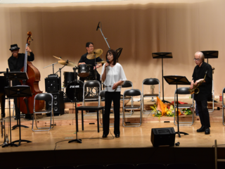 歌を歌う女性と後ろでコントラバス、ドラム、ギターを演奏している写真