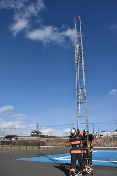 下した梯子を立ち上げ、隊員2人が向き合い1人が梯子を支え、1人が最高位置まで梯子を伸ばしている写真