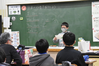 馬頭小５年の男子児童が葉書に好きな四季を英語と絵で書き、ビデオカメラに向かい英語で紹介している