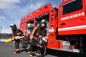 消防車側面に収納のホースを取り出し消火現場に向かう隊員２人